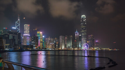 Obraz premium Hong Kong city skyline at night over Victoria Harbor with cloudy sky and urban skyscrapers timelapse hyperlapse.