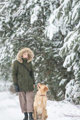 Beautiful young girl walking with a purebred retriever near a snowy forest in winter.