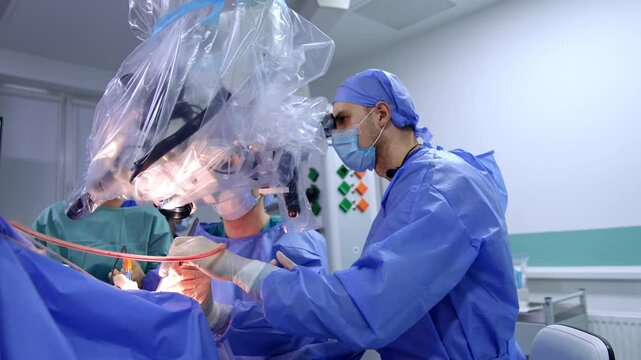 Surgeons in blue uniforms sit at microscope performing operation. Progress of neurosurgery in modern hospital.
