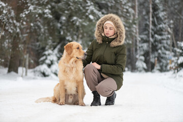 Beautiful young girl walking with a purebred retriever near a snowy forest in winter.