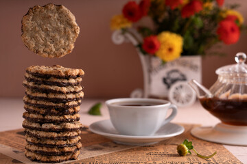 photo Delightful Moment with Stack of Oatmeal Cookies Complemented by Freshly Brewed Tea and Vibrant Floral Arrangement for Cozy, Relaxed Afternoon Break.