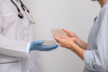 doctor and patient, exam, consultation in clinic office, holding breast enlargement implant in...