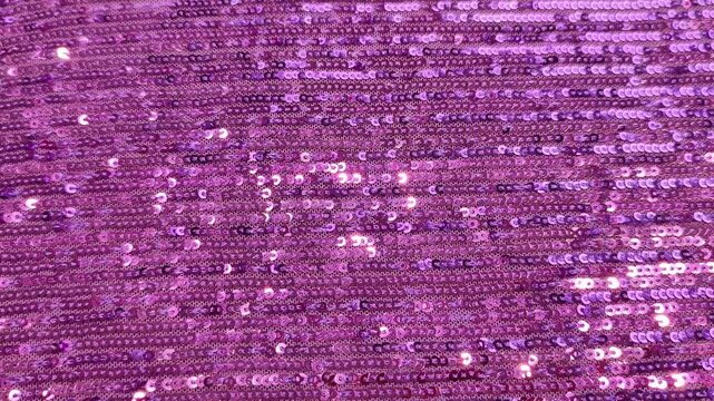 Close-up view of a sparkling pink sequin fabric with a textured, shimmering surface pattern