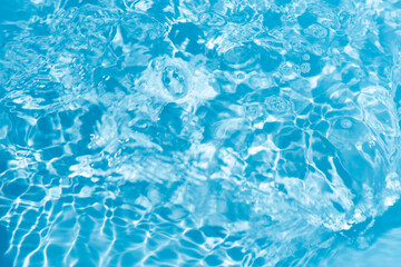 Blue water with ripples on the surface. Defocus blurred transparent blue colored clear calm water surface texture with splashes and bubbles. Water waves with shining pattern texture background.