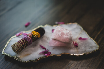 burnt sage smudge stick on crystal platter with rose quartz and flowers