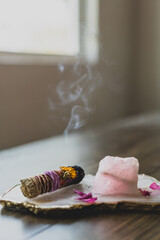 burning sage stick on crystal platter on wood table in front of window