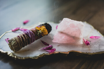 closeup of sage bundle with crystals and flower petals on wood table