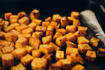 Baked pumpkin cubes with spices and olive oil on parchment paper.