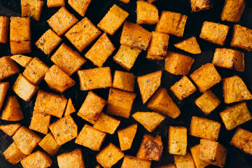 Baked pumpkin cubes with spices and olive oil on parchment paper, top view.