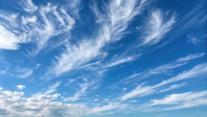 Thin and wispy white clouds are suspended in the clear blue sky on a sunny day, airy, optimistic, joyful