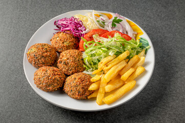 plate of falafel with chips and vegetables on a gray stone table isolated 