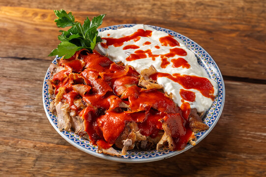 Turkish iskender kebab dish with beef, spices, yogurt, and tomato sauce served in a dish and resting on a rustic wooden table 