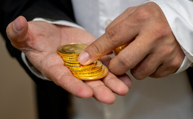 Close-up of a man's hands in a business suit handling real gold coins. The image emphasizes wealth, finance, and investment, showing a stack of shiny, valuable currency.