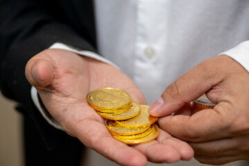 Close-up of a man's hands in a business suit handling real gold coins. The image emphasizes wealth, finance, and investment, showing a stack of shiny, valuable currency.