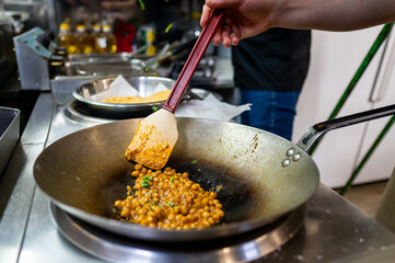 A close-up shot of a person cooking chickpeas in a wok with a spatula. The image captures the vibrant colors and textures of the ingredients, highlighting the process of preparing a delicious meal