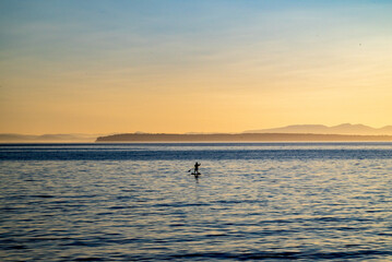 Fototapeta premium Silhouette of a paddle boater on the water at sunset.