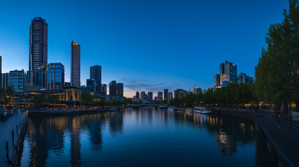 Fototapeta premium Modern city skyline at dusk reflecting on river under a clear blue sky.