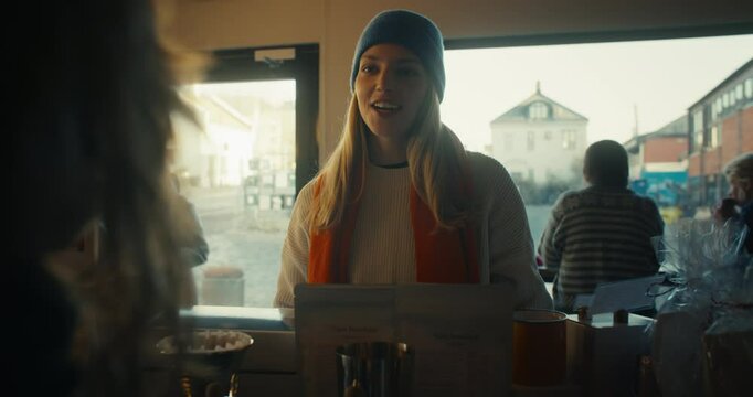 A female customer and woman barista or cafe owner have a friendly chat and interaction over the counter. Staff employee and customer ordering drinks, get served tea in scandinavian cafe