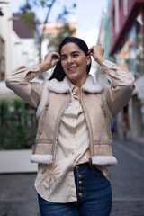 Stylish woman in beige vest and jeans, fixing her hair as she strolls through the city