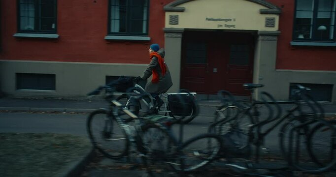 Side panning shot of young woman cycling on long tail electric cargo bike through scandinavian city street. Cinematic image of urban sustainable green mobility and nordic lifestyle