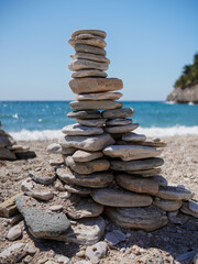 A stacked arrangement of smooth stones on a sandy beach with the sea and waves in the background, capturing a sense of calm and natural balance under a clear blue sky.