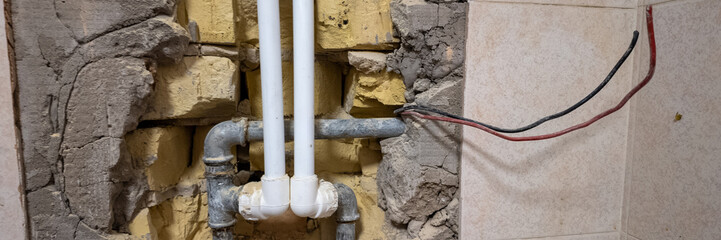 Exposed plumbing and wiring in a damaged wall illustrate home renovation challenges and construction issues