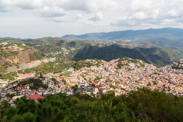 Fototapeta premium Aerial panoramic view over Pueblo Magico of Taxco, one of Mexico's most scenic towns with Santa Prisca church and a scenic mountainous landscape. Taxco, Guerrero, Mexico