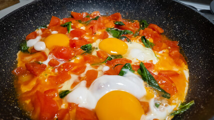 A vibrant dish of shakshuka with fresh tomatoes, eggs, and greens in a skillet, perfect for a Mediterranean breakfast