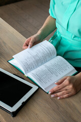 Fototapeta premium A Caucasian woman reads sheet music from a book beside a tablet, embodying creativity and learning for World Music Day