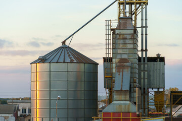 Grain silo elevator at sunset against the background of clouds. Iron barrels for grain storage. The harvest season.
