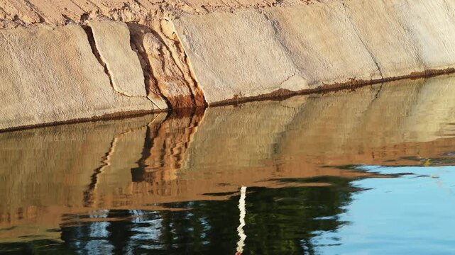 The crumbling concrete bank of a water-filled canal in the morning, part of the Central Arizona Project in Phoenix, Arizona