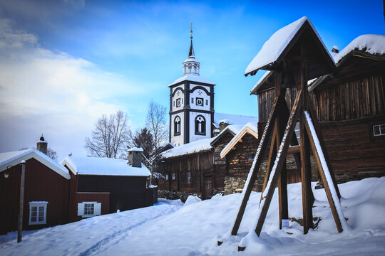 Røros Church tower rises above a snowy landscape under a clear blue sky, showcasing the winter charm of this historic Norwegian town
