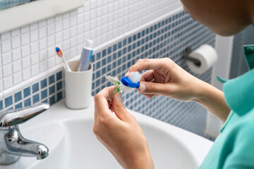 A teenage boy cleans his dental retainer with a toothbrush, seen in a bathroom mirror, focusing on...