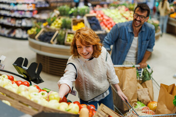 Cheerful couple buying groceries in supermarket picking fresh vegetables