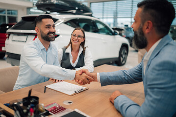 Content pair shaking hands with dealer after closing car deal.