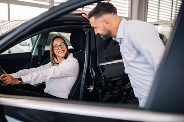 Happy customer inspects vehicle interior with friendly salesman.