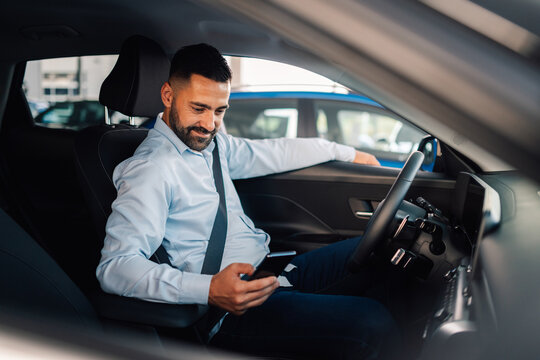 Man smiling in car holding phone, parked in modern environment