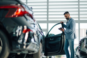 Man checking car features in dealership using a digital tablet.