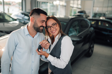 Couple enthusiastically holding car key in dealership.