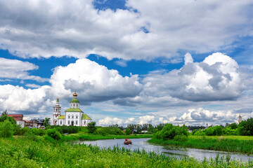 SUZDAL, RUSSIA - Beautiful landscape of Suzdal overlooking the Kamenka River and the ancient Russian Church of Elijah the Prophet (Elijah Church). An ancient boat floats on the river
