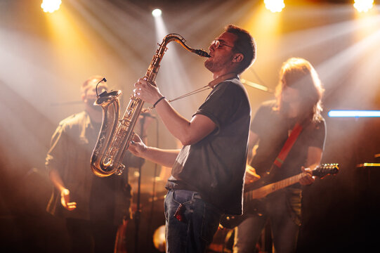 Saxophonist playing sax on stage with band during concert