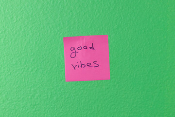 Pink Sticky Note with 'Good Vibes' Message on Green Wall