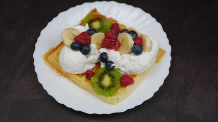 Waffles with whipped cream, blueberries, bananas, raspberries, and kiwi