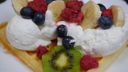 Waffles with whipped cream, blueberries, bananas, raspberries, and kiwi