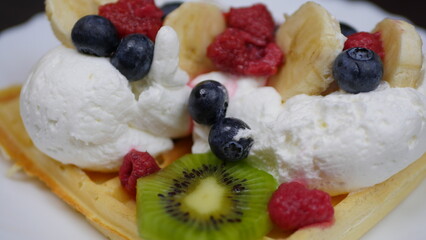 Waffles with whipped cream, blueberries, bananas, raspberries, and kiwi