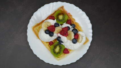 Waffles with whipped cream, blueberries, bananas, raspberries, and kiwi