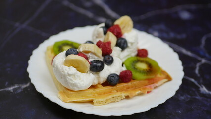Waffles with whipped cream, blueberries, bananas, raspberries, and kiwi