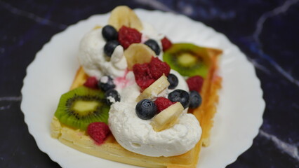 Waffles with whipped cream, blueberries, bananas, raspberries, and kiwi