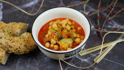 A dish of chickpeas, peppers, carrots and other vegetables with a whole grain roll