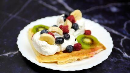 Waffles with whipped cream, blueberries, bananas, raspberries, and kiwi